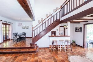 A spacious dining area with a wooden staircase, a bar area with stools, and a view of the outdoors.