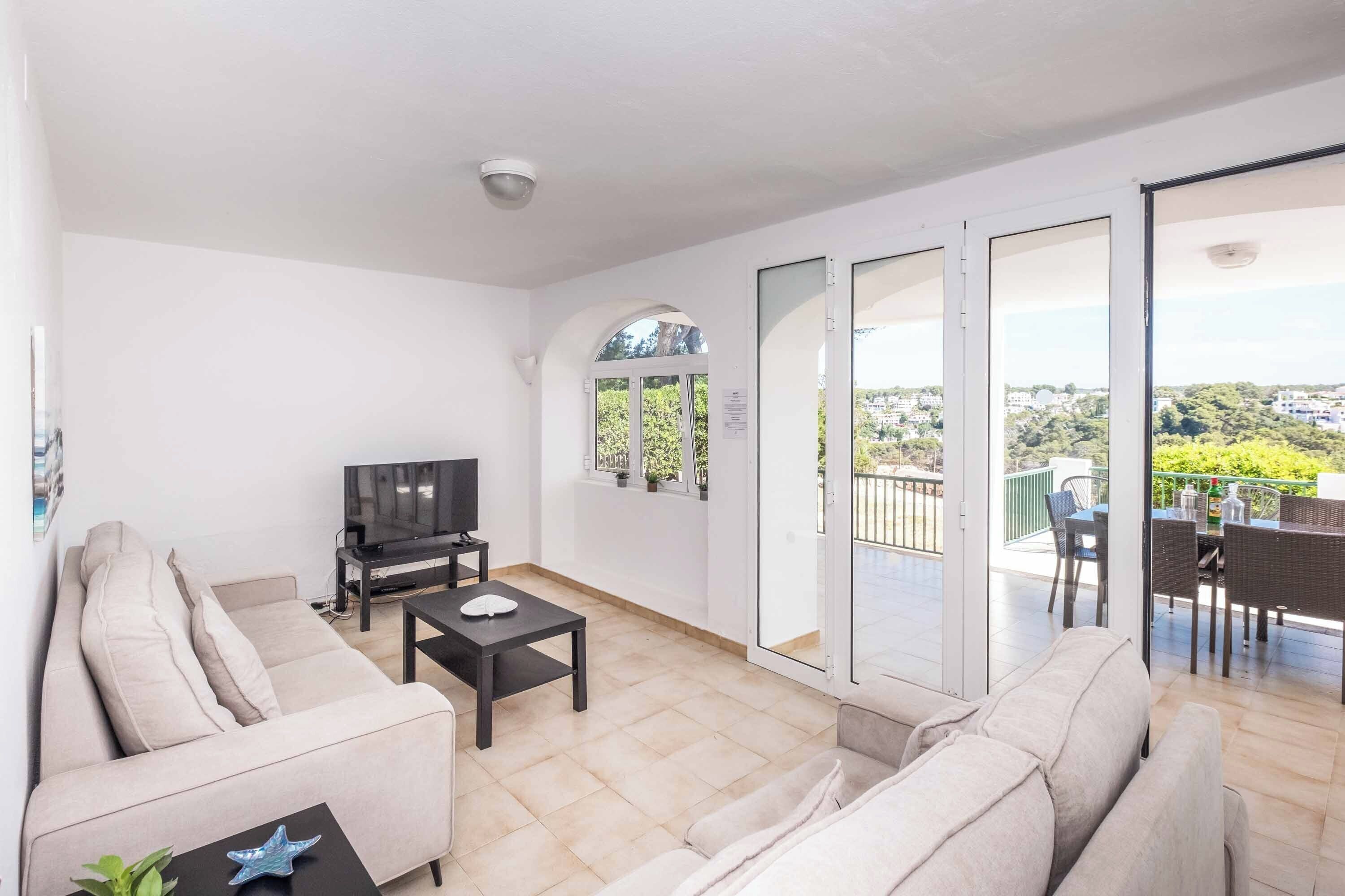 A modern living room with a sofa, a coffee table, a TV, and a balcony with a dining area.