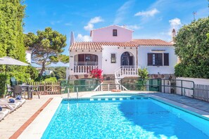 Zona de piscina con sillones de descanso y una escalera que conduce a un edificio con tejado de baldosas.