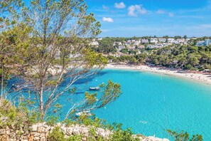 Une vue sur la côte, avec une eau turquoise cristalline, un rivage rocheux et des bâtiments en arrière-plan.