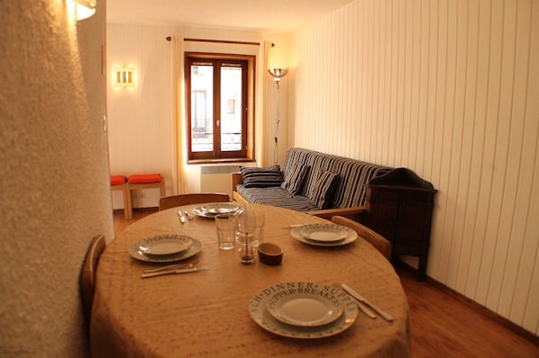 A dining area with a table set for dinner, a sofa, and a window with curtains. - Fantastic location in the heart of Chamonix, a large studio great option for couples or families (Chamonix-Mont-Blanc)