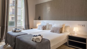 Hotellihuone, jossa on kaksi sänkyä, suuri seinälle asennettu taideteos, yöpöytä lampun kanssa ja näkymä ulkopuolella olevalle parvekkeelle.