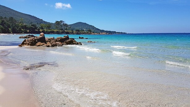 A beach with clear turquoise water, rocky formations, and a hilly landscape in the background. - Terraced house with 3 bedrooms and garden, only 100m. from the beach (Grosseto-Prugna)