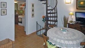 A dining area with a round table, chairs, and a staircase leading to an upper level. - Terraced house with 3 bedrooms and garden, only 100m. from the beach (Grosseto-Prugna)