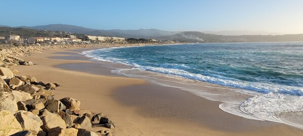 Una playa con costa rocosa, olas y un pueblo lejano.