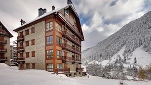 Ein mehrstöckiges Hotel mit Fassade aus Stein und Holz, mehreren Balkonen und einem verschneiten Berggipfel im Hintergrund.