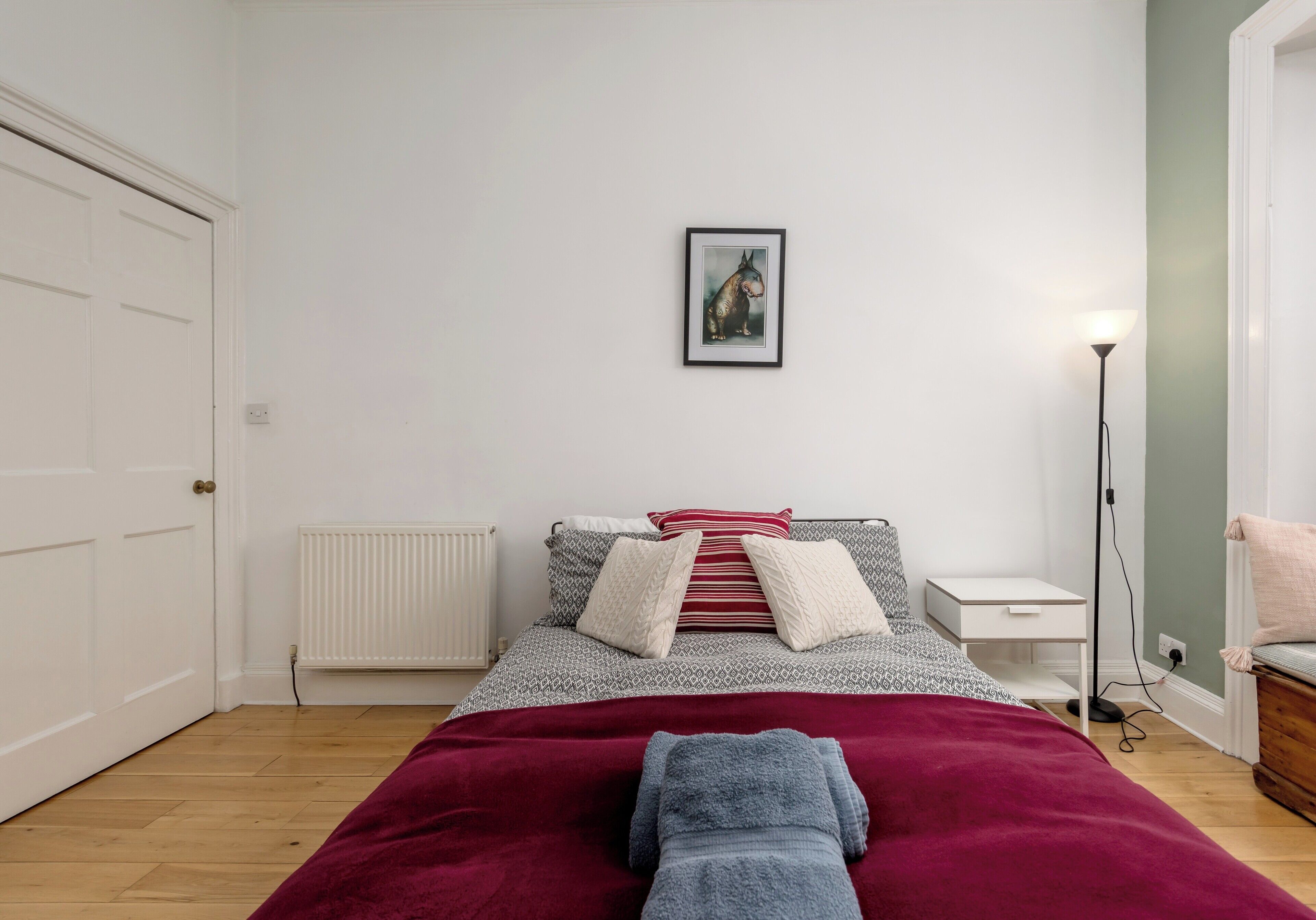 Un dormitorio con cama, un cuadro enmarcado en la pared, una mesita de noche y una lámpara de pie.