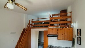 Una cucina compatta con mobili in legno, un piano cottura integrato e un lavandino piccolo, e una scala che conduce a una zona mansardata.