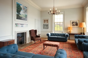 A room with a fireplace, blue sofas, a patterned rug, and artwork on the walls. - The Merchant's House (Eyemouth)