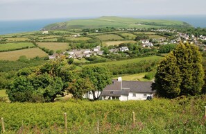 Un paysage rural avec une maison blanche entourée de verdure et de champs, dominant un village et la mer.