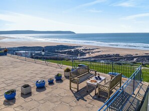 A terrace with outdoor seating, potted plants, and a view of the beach and ocean.