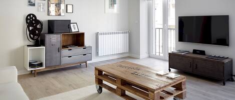 Een moderne woonkamer met een houten salontafel, een grijze kast, een witte bank en een flatscreen televisie.