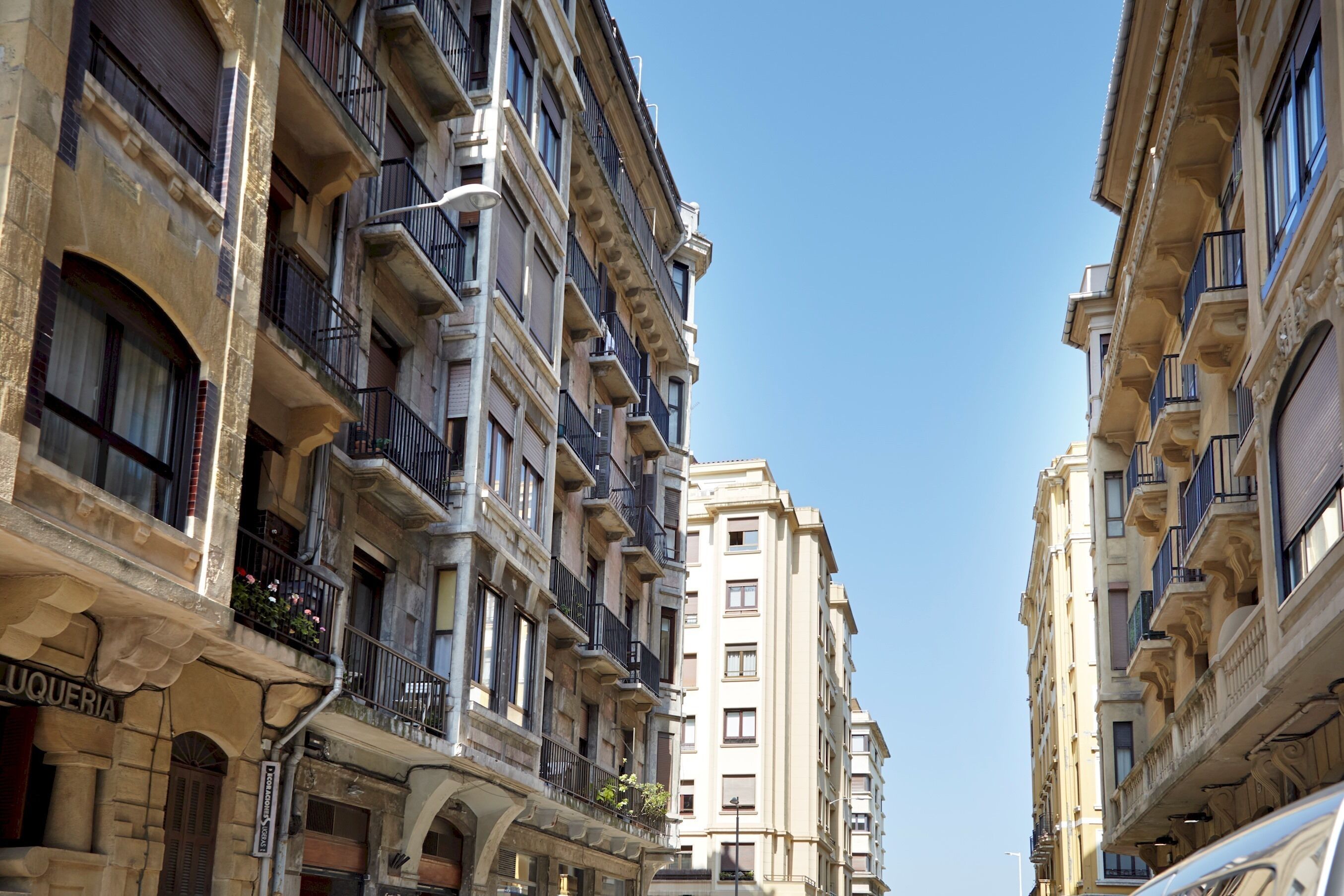 A narrow street flanked by multi-story buildings with balconies and a clear blue sky.