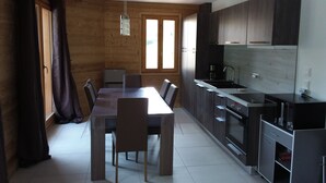 Cozinha moderna com armários de madeira escura, uma pia de aço inoxidável e um forno embutido. Há uma mesa de jantar com cadeiras no centro do quarto.
