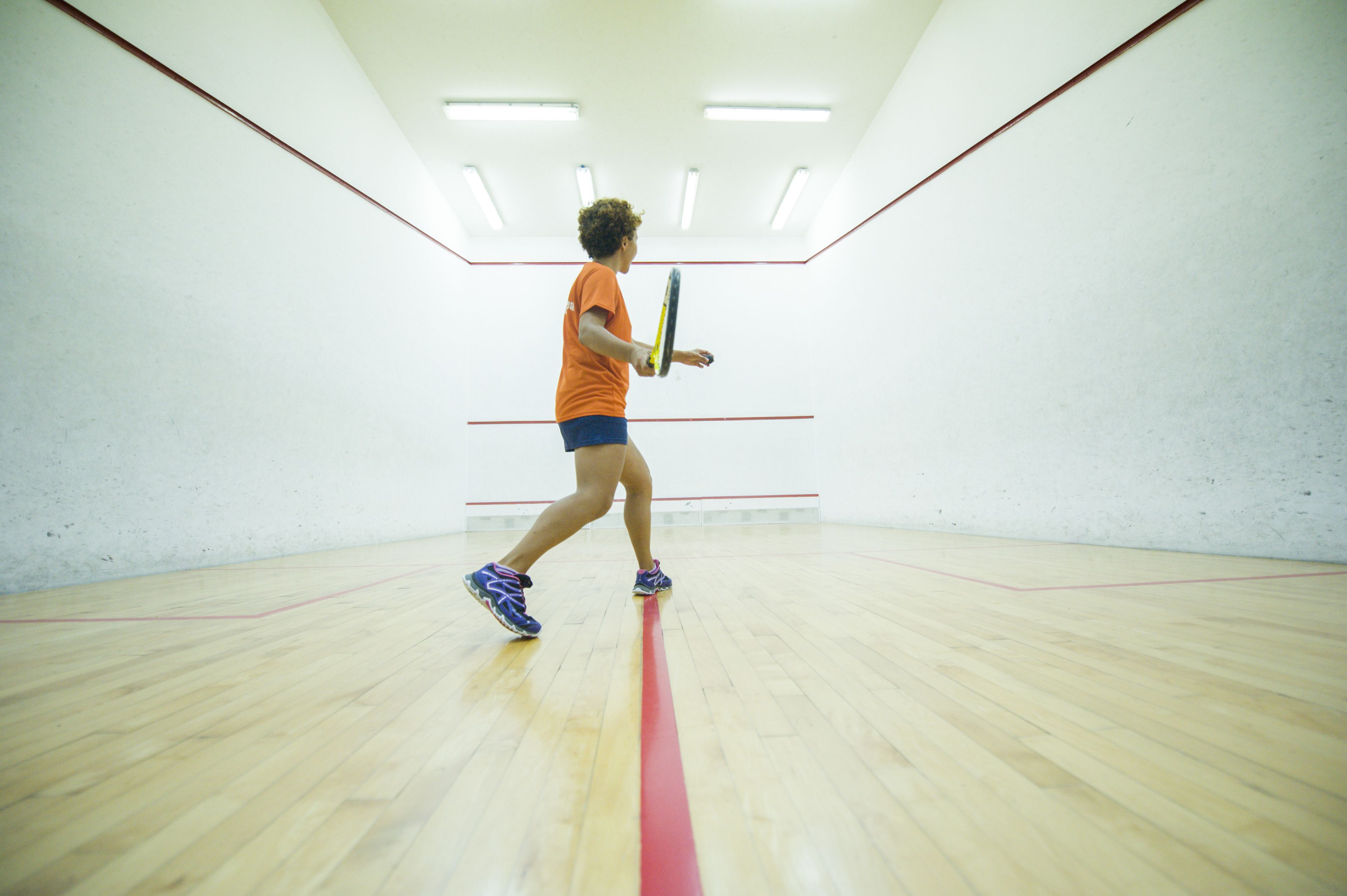 Una cancha de squash con piso de madera y líneas divisorias rojas.