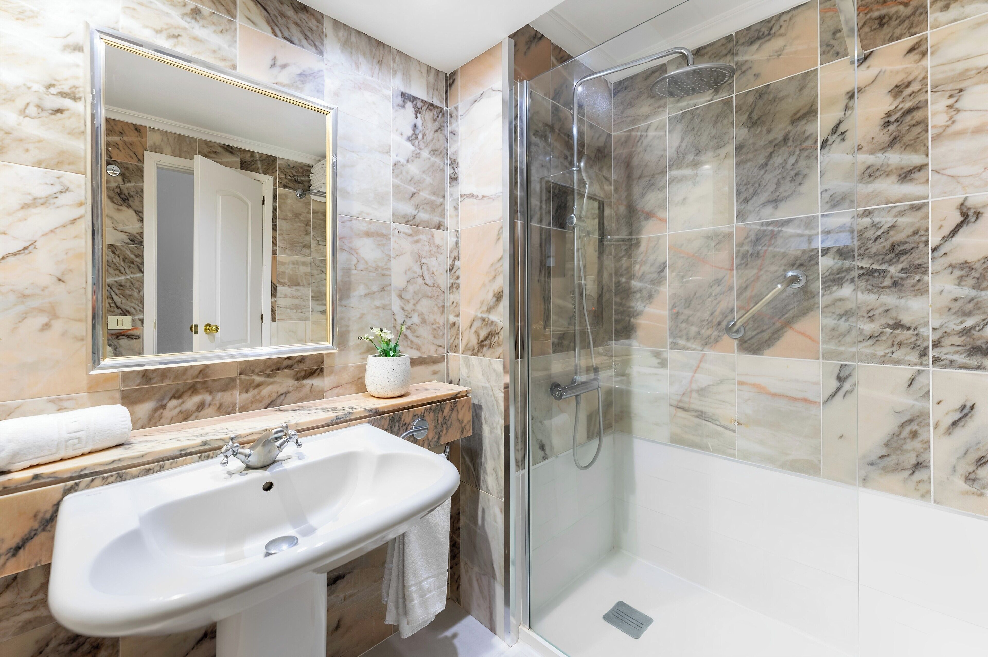 Une salle de bain avec une douche carrelée de marbre, un lavabo et un miroir.