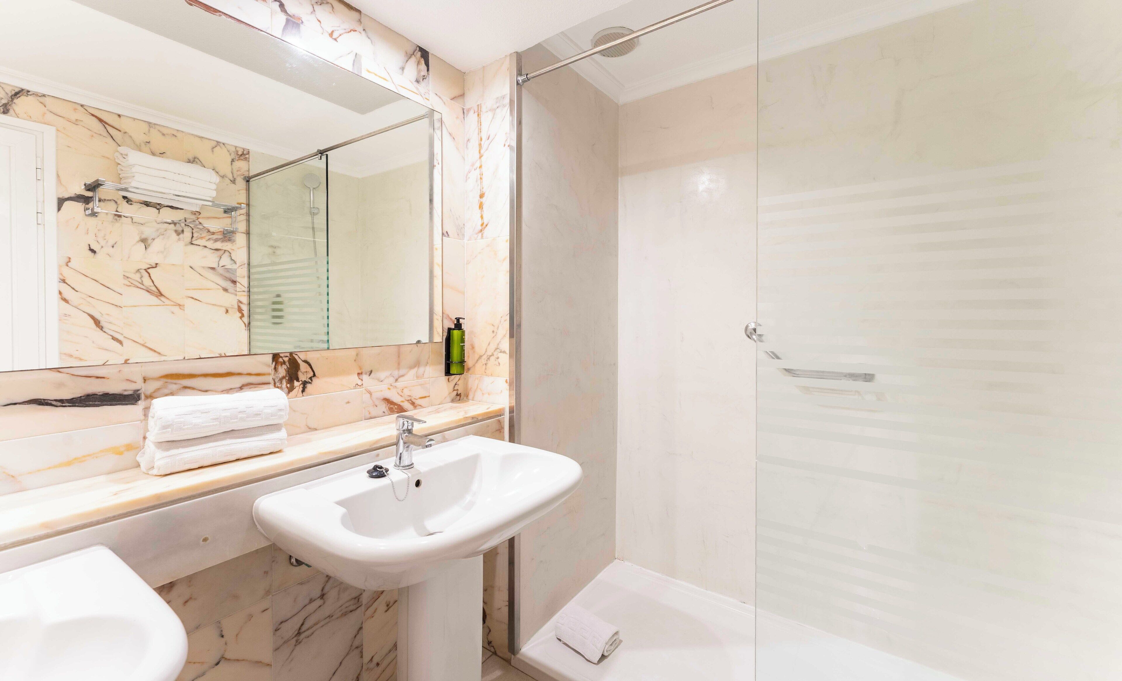 Un baño con dos lavamanos, un espejo grande y una ducha con mampara de cristal.