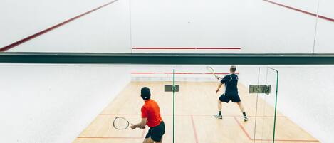 A squash court with two players, one in red and one in black, playing.
