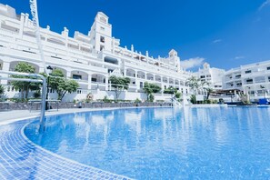 Un grande hotel bianco a più piani con una piscina in primo piano.