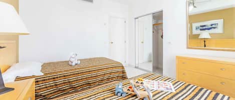 A hotel room with a bed, a small table, a lamp, a dresser, and a toy car.