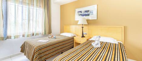 A hotel room with two beds, a nightstand, a lamp, and a painting on the wall.