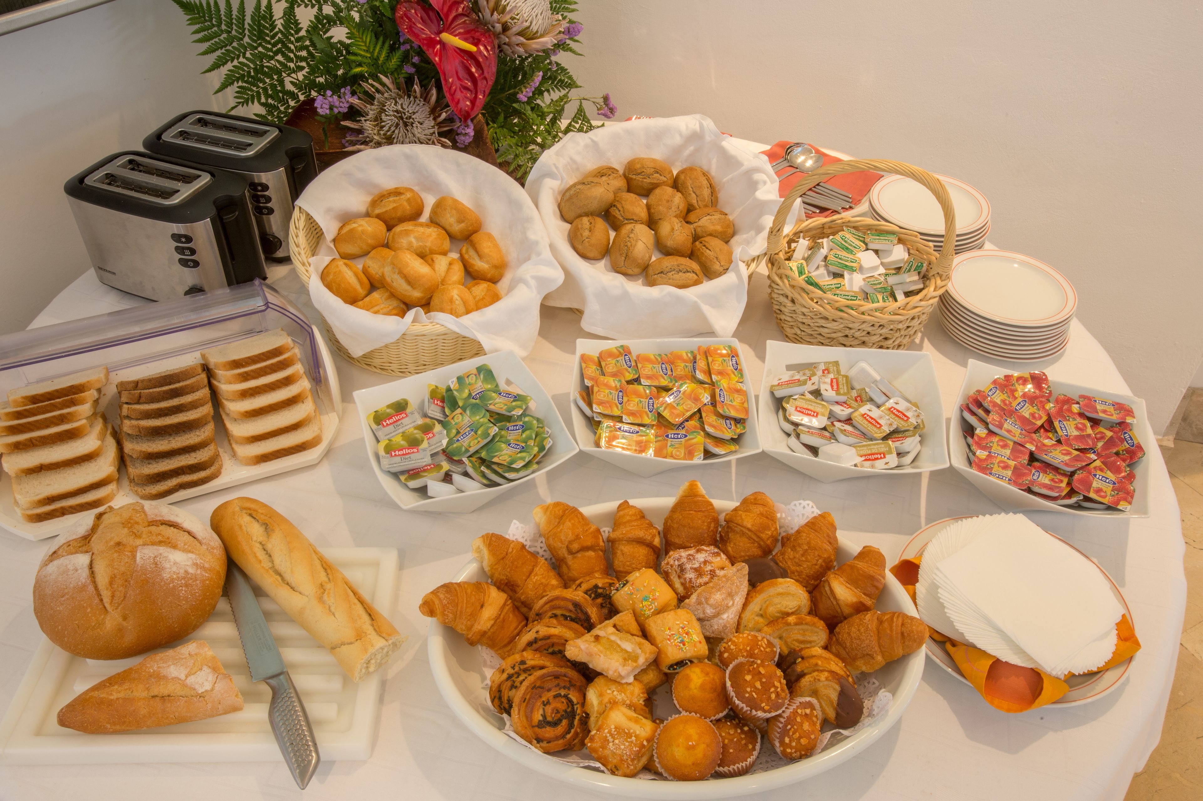 Une table de buffet proposant divers aliments, notamment du pain, des pâtisseries et des condiments.