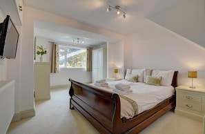 A bedroom with a large bed, bedside tables, a TV, and a window with curtains. - 4 Bed in Braunton (oc-anchor) (Croyde)