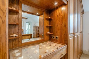 Un meuble-lavabo en bois pour la salle de bain, doté d’un miroir, d’étagères et d’un plan de travail où sont exposés des coquillages.