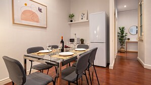 Un comedor moderno con una mesa de vidrio, cuatro sillas grises, un refrigerador blanco y un microondas.