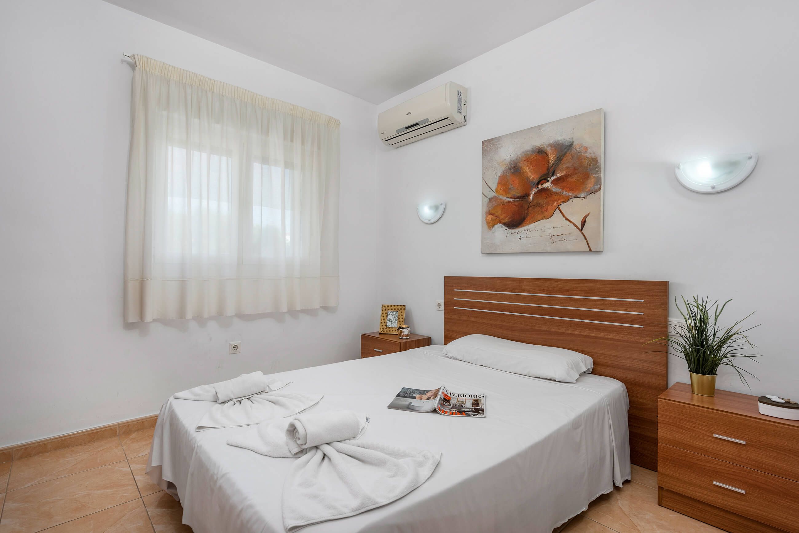 A bedroom with a bed, a nightstand, a potted plant, and a painting on the wall.