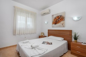 A bedroom with a bed, a nightstand, a potted plant, and a painting on the wall.