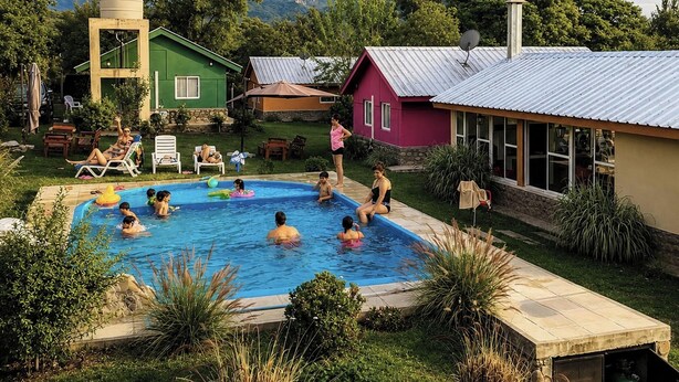 Una piscina rodeada de casas, con gente nadando y descansando.