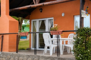 An outdoor patio with white plastic chairs and a table, a wooden pergola, and a sign with a bird. - El Tucán Cabin – Nature and Tranquility near Salta (Vaqueros)