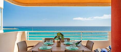 A balcony with a table set for two, overlooking a turquoise sea.
