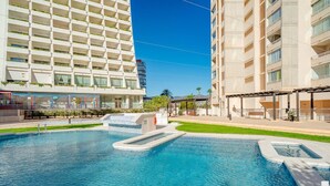 A swimming pool with a small waterfall feature, surrounded by a well-maintained lawn and a multi-story building with balconies. - Apolo XVI 2 4 19 - Grupo Turis - Calpe, Costa Blanca (Calpe)
