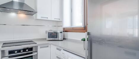A modern kitchen with a stainless steel range hood, a built-in oven, a microwave, and a washing machine.