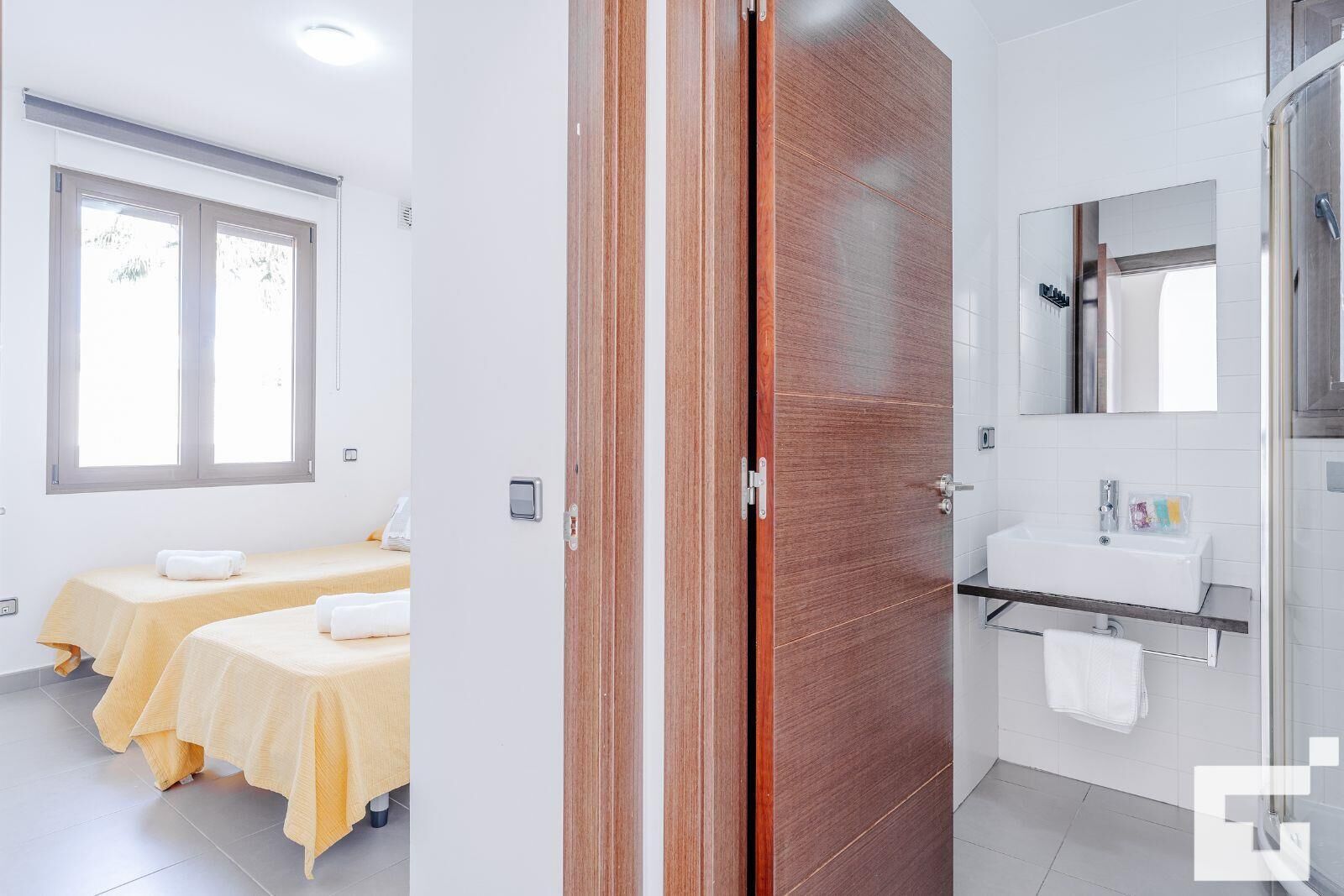Ein Hotelzimmer mit zwei Betten, einem Badezimmer mit Waschbecken und Spiegel sowie einem Fenster mit Jalousien.