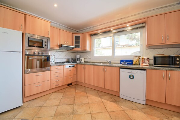 A kitchen with wooden cabinets, a dishwasher, an oven, a microwave, and a window providing natural light. - Anngo 6 pax - Javea, Costa Blanca (Javea)