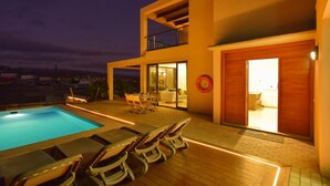 Una casa moderna con piscina, mobiliario de exterior e interior bien iluminado.