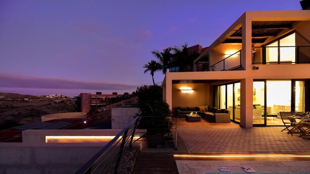 Una casa moderna de dos pisos con piscina, mobiliario exterior y vistas al paisaje.