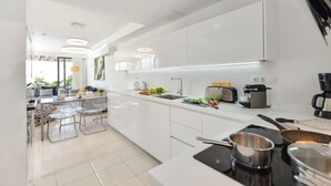 Una cocina moderna con armarios blancos, una isla central y un comedor con sillas traslúcidas.
