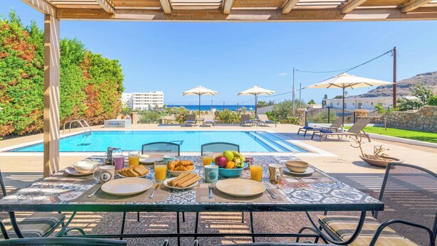 Un coin petit-déjeuner aménagé au bord de la piscine, avec une table, des chaises et des parasols.