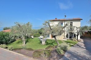A two-story house with a tiled roof, a satellite dish, and a well-maintained lawn with a few trees and a stone pathway.