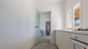 Un pasillo estrecho con una puerta de vidrio que da a un comedor, una cocina con armarios blancos y un ventanal con vistas al exterior.