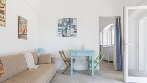 Una habitación con un sofá color beige, una mesita azul pequeña y una silla de madera.