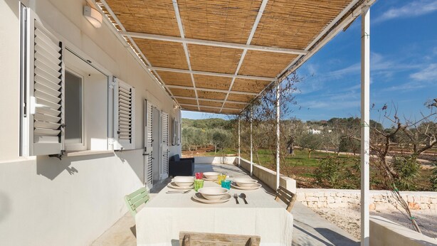 Un patio al aire libre con una mesa lista para comer, una zona de estar cubierta y vistas del paisaje circundante.