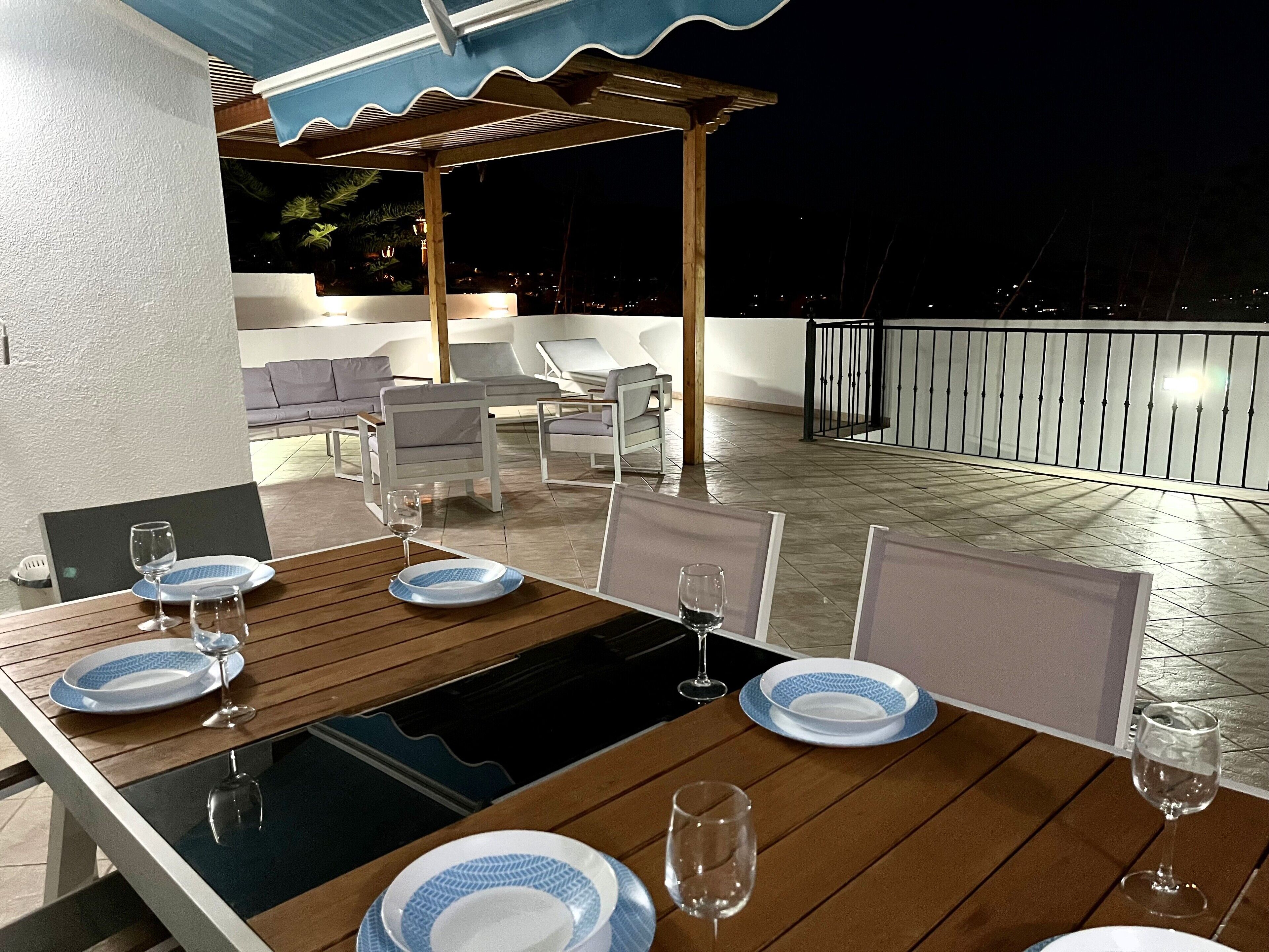 Una terraza en la azotea con una mesa de madera dispuesta para comer, con platos blancos y azules y copas de vino.