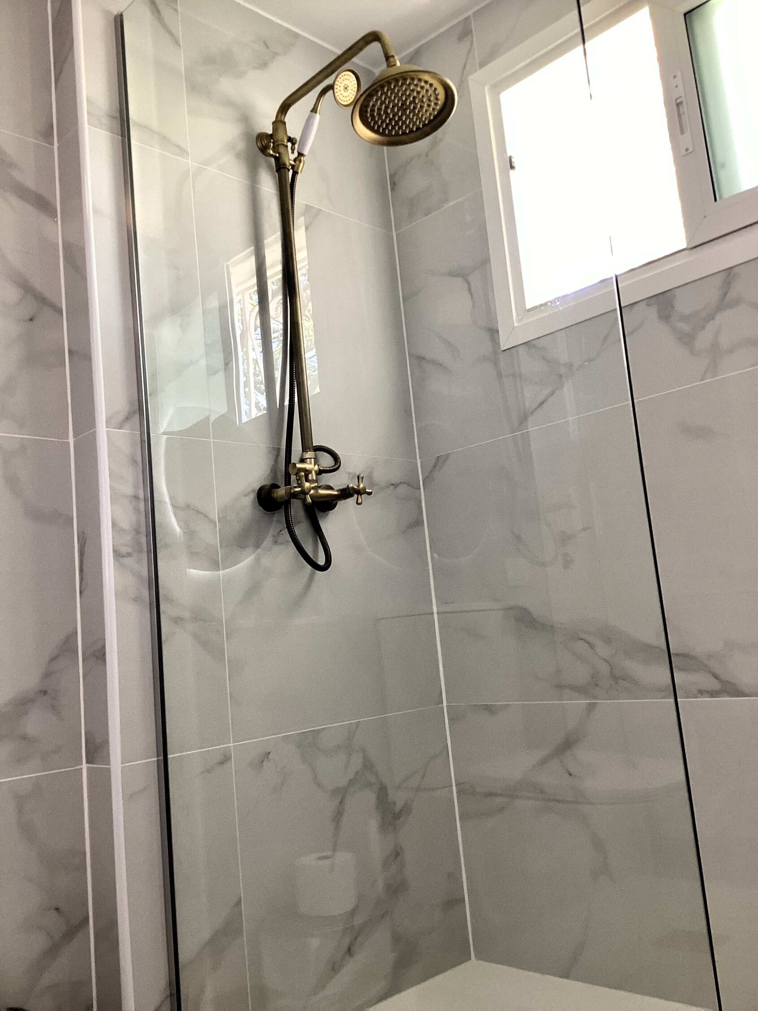 Eine Dusche mit Handbrause und fest installierter Duschköpfe, an einer Wand mit einem Fenster darüber.