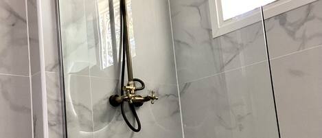 Eine Dusche mit Handbrause und fest installierter Duschköpfe, an einer Wand mit einem Fenster darüber.