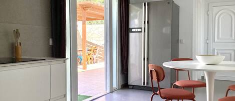 Eine moderne Küche mit Backofen, ein Essbereich mit weißem Tisch und roten Stühlen sowie eine Glastür, die auf eine Terrasse im Freien führt.